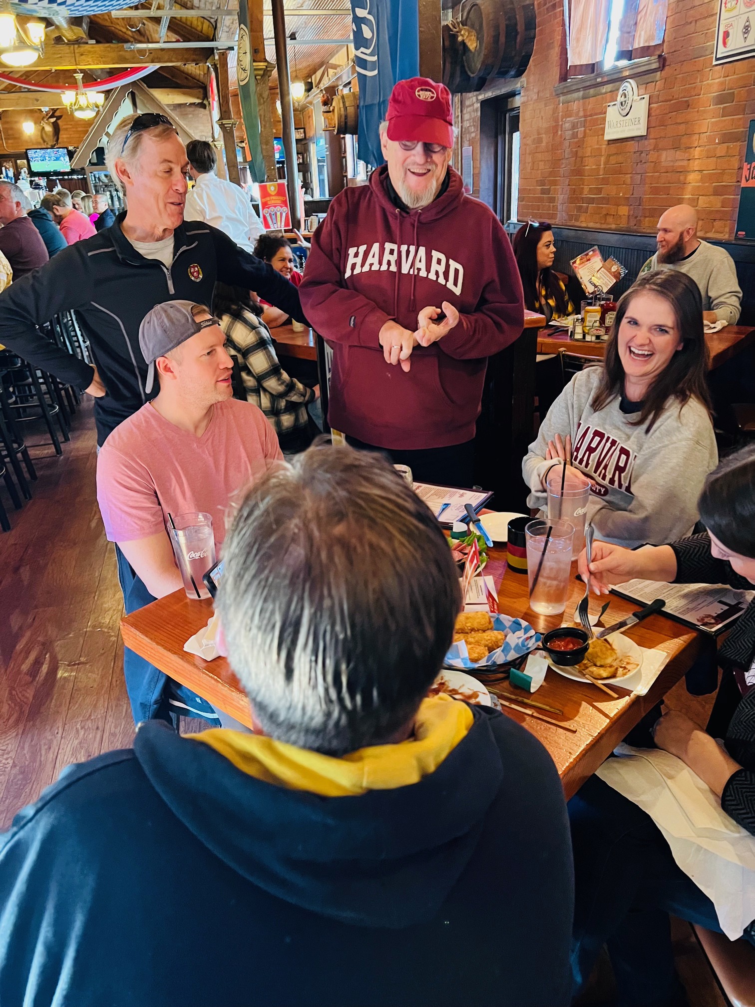 Harvard Club of Iowa members gathered at a table in a bar, chatting and laughing.